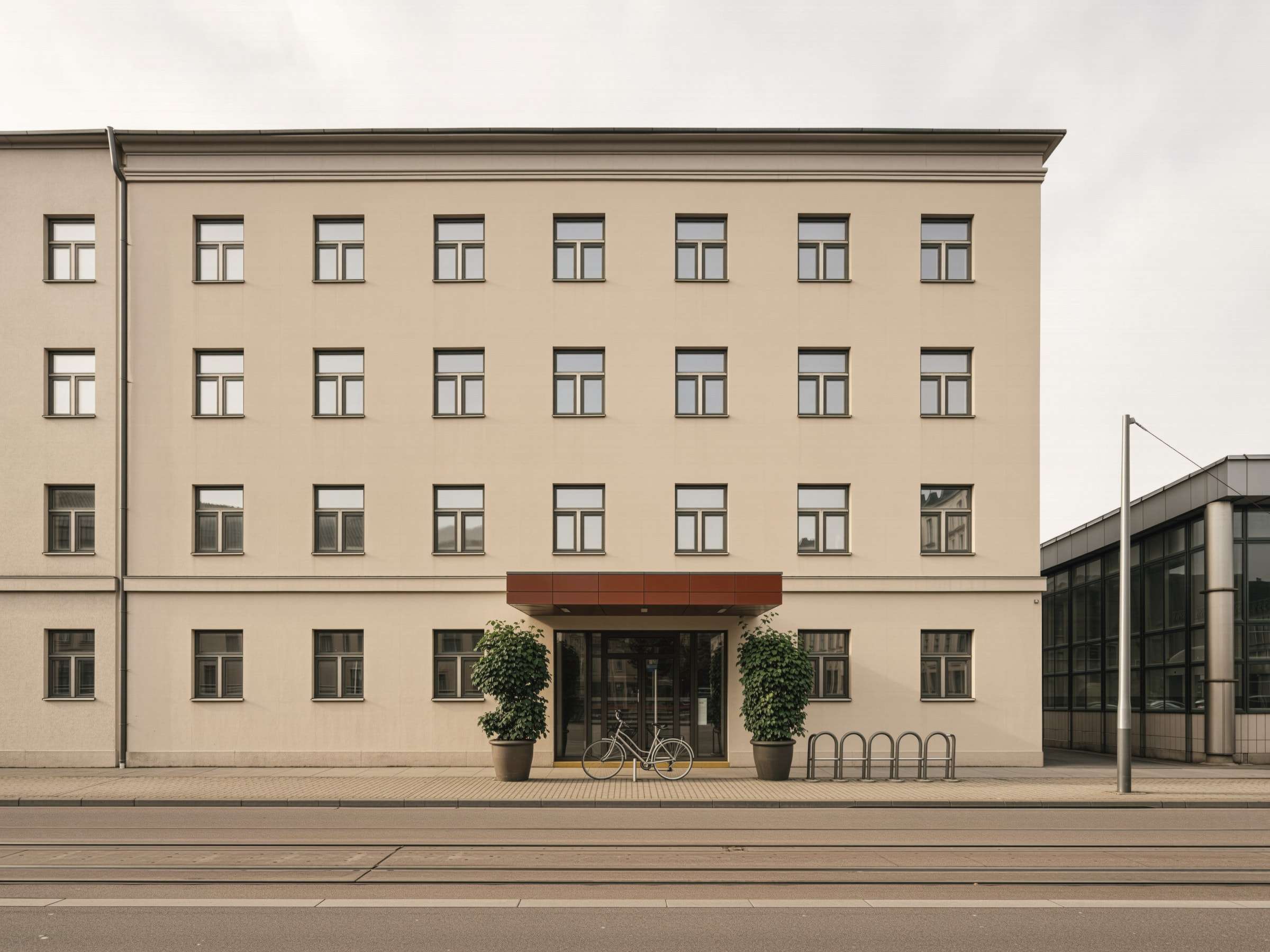 Visualisierung: viergeschossiges Stadthotel mit heller Putzfassade und ziegelrotem Eingangsvordach an einer Straße mit Straßenbahnschienen