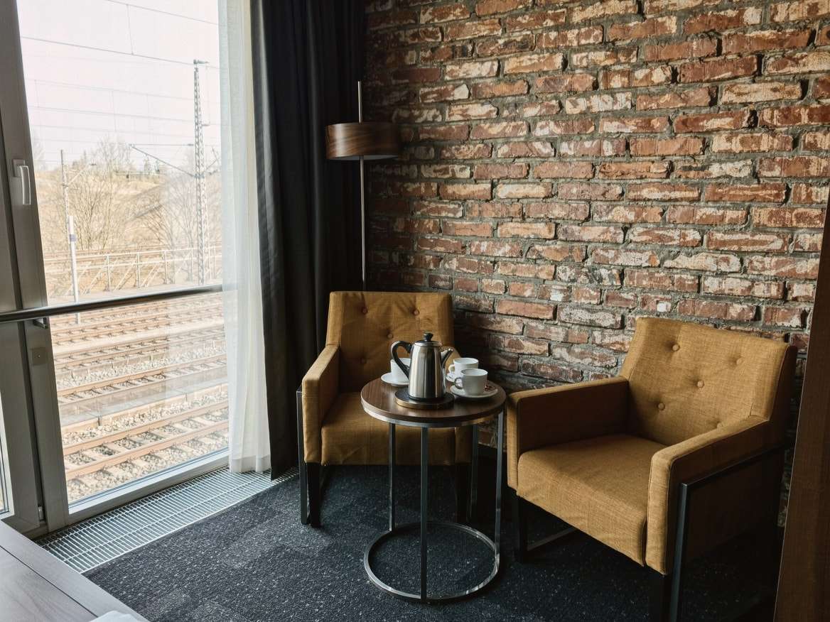Komfort-Doppelzimmer: zwei senfgelbe Sessel und ein kleiner Tisch mit Kanne und Tassen am Fenster, dahinter eine Backsteinwand